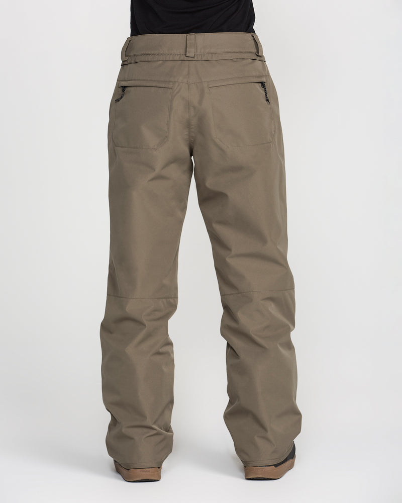 A person is shown from the back, wearing Volcom Women’s Coldfront Insulated Baggy Pants in a khaki color, featuring two zippered back pockets and belt loops, paired with brown shoes, all set against a plain white background.