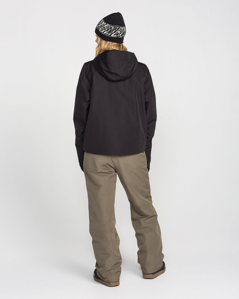 A person wearing a black jacket, a pair of Volcom Women’s Coldfront Insulated Baggy Pants in olive green, and a black beanie stands facing away from the camera against a plain white background.