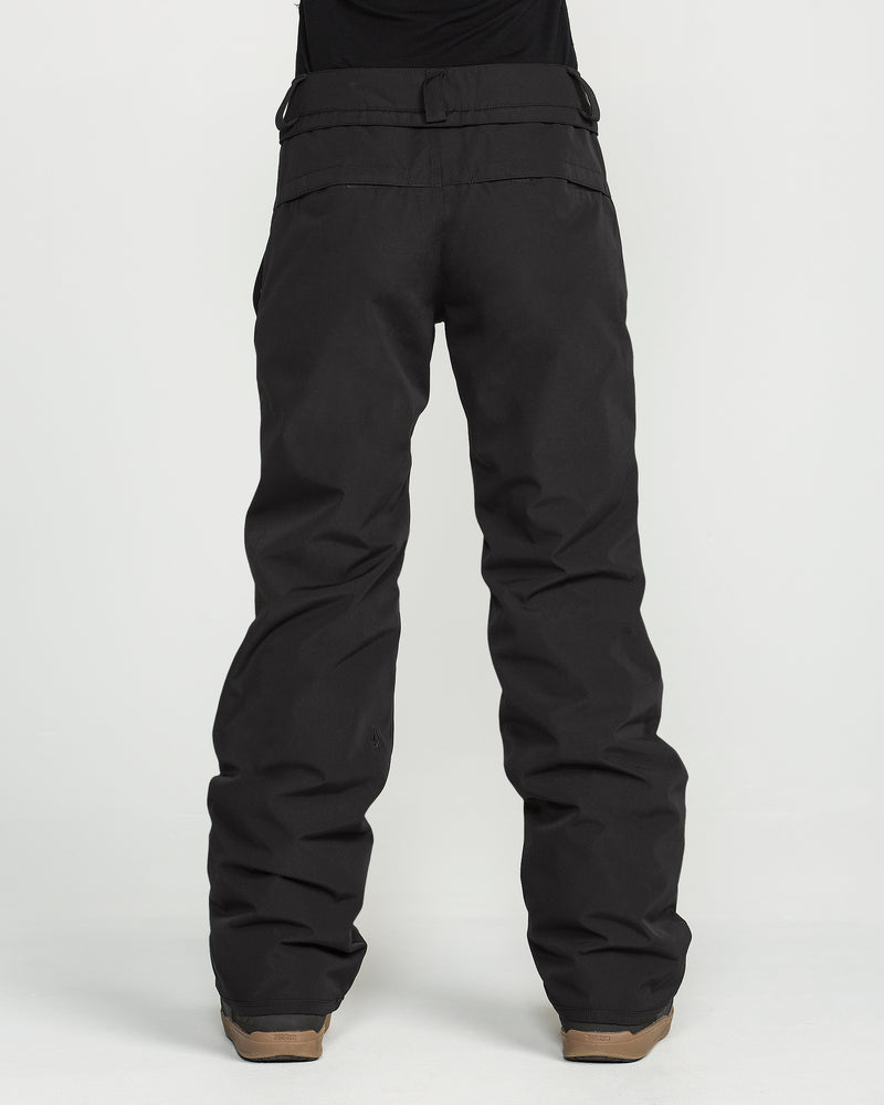 A person is shown from the waist down, wearing Volcom Women’s Stoned Insulated Pants in black paired with brown boots, standing against a plain white background. These 10K waterproof pants are designed for comfort and performance; the upper body is mostly out of frame.