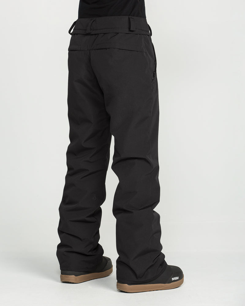 A person wearing loose-fitting black Volcom Women’s Stoned Insulated Pants and black snow boots stands on a white background with their back facing the camera.