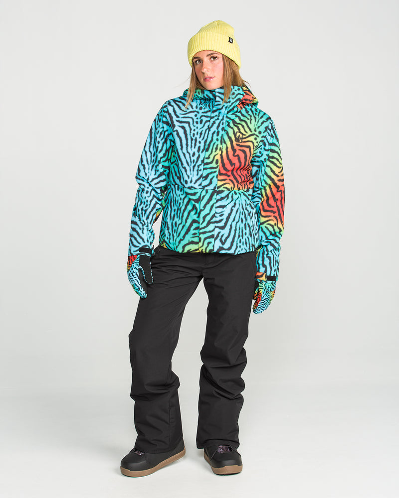 A person wearing a yellow beanie, a colorful zebra-striped jacket, Volcom Women’s Stoned Insulated Pants, and gloves stands against a plain white background.