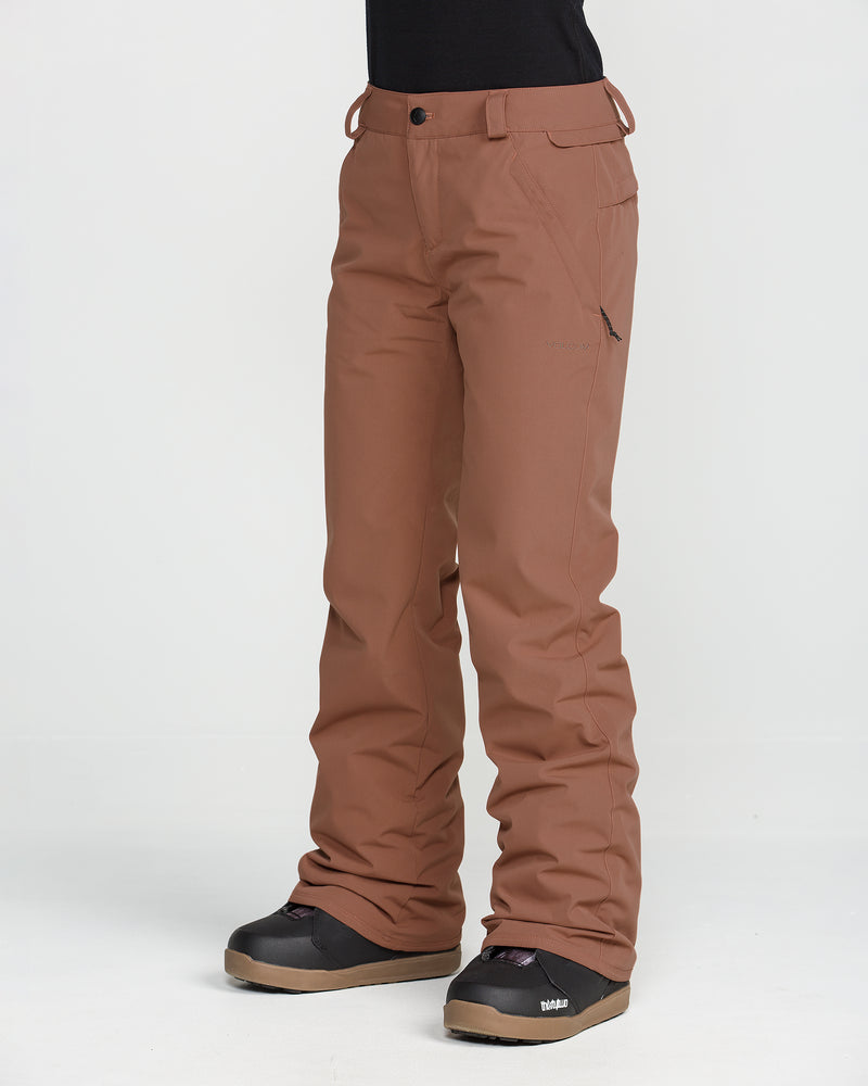A person is wearing Volcom Women’s Stoned Insulated Pants in brown and black boots, standing against a plain white background. The image focuses on the lower body to highlight the pants’ 10K waterproof rating and recycled insulation, with nothing visible above the waist.