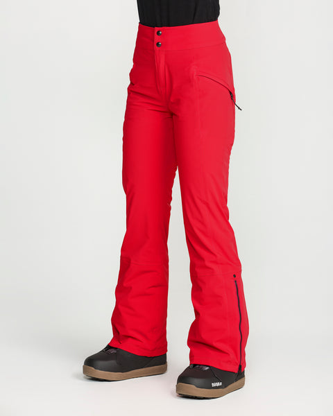 A person is wearing bright red Volcom Women’s Alpine All Day Insulated Pants and black snow boots, standing against a plain white background. These high-rise fit pants feature zippered pockets, flared legs, and two visible buttons at the waist, and are crafted with 4-way ultra stretch fabric for all-day comfort on or off the slopes.