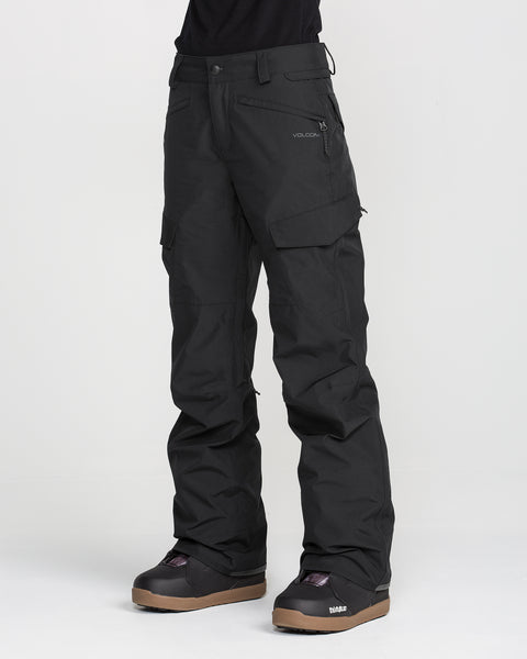 A person is wearing black Volcom Women’s Stonelark GORE-TEX Pants and black snow boots, standing against a plain white background. Only the lower half of the body is visible.