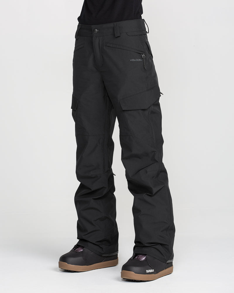 A person is wearing black Volcom Women’s Stonelark GORE-TEX Pants and black snow boots, standing against a plain white background. Only the lower half of the body is visible.