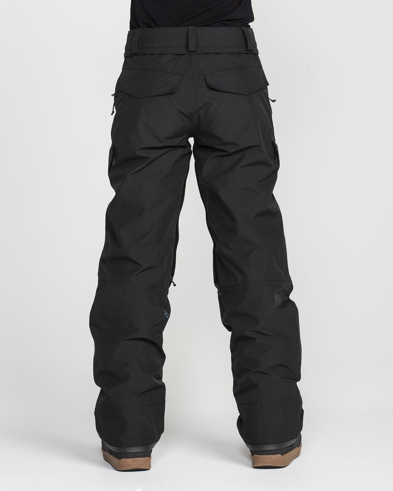 A person is shown from the back against a plain white background wearing Volcom Women’s Stonelark Gore-Tex Pants in black and brown boots. The loose-fitting waterproof pants feature back pockets with flaps, a slightly wrinkled texture, and are designed to be breathable and functional for outdoor activities.