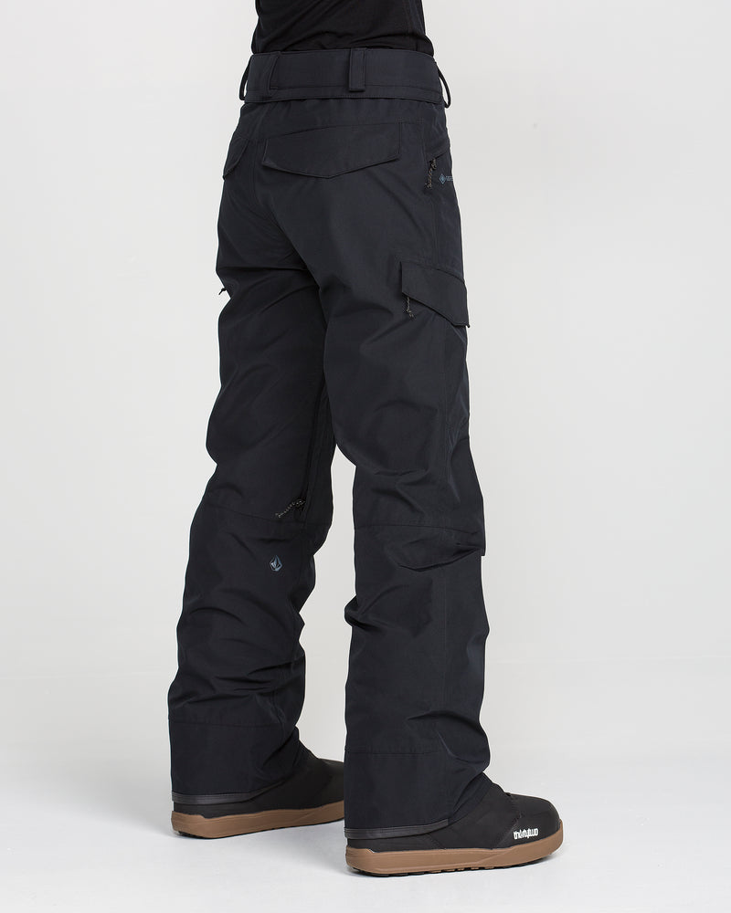A person wearing Volcom Women’s Stonelark Gore-Tex Pants in black and black boots stands against a plain white background, facing away from the camera.