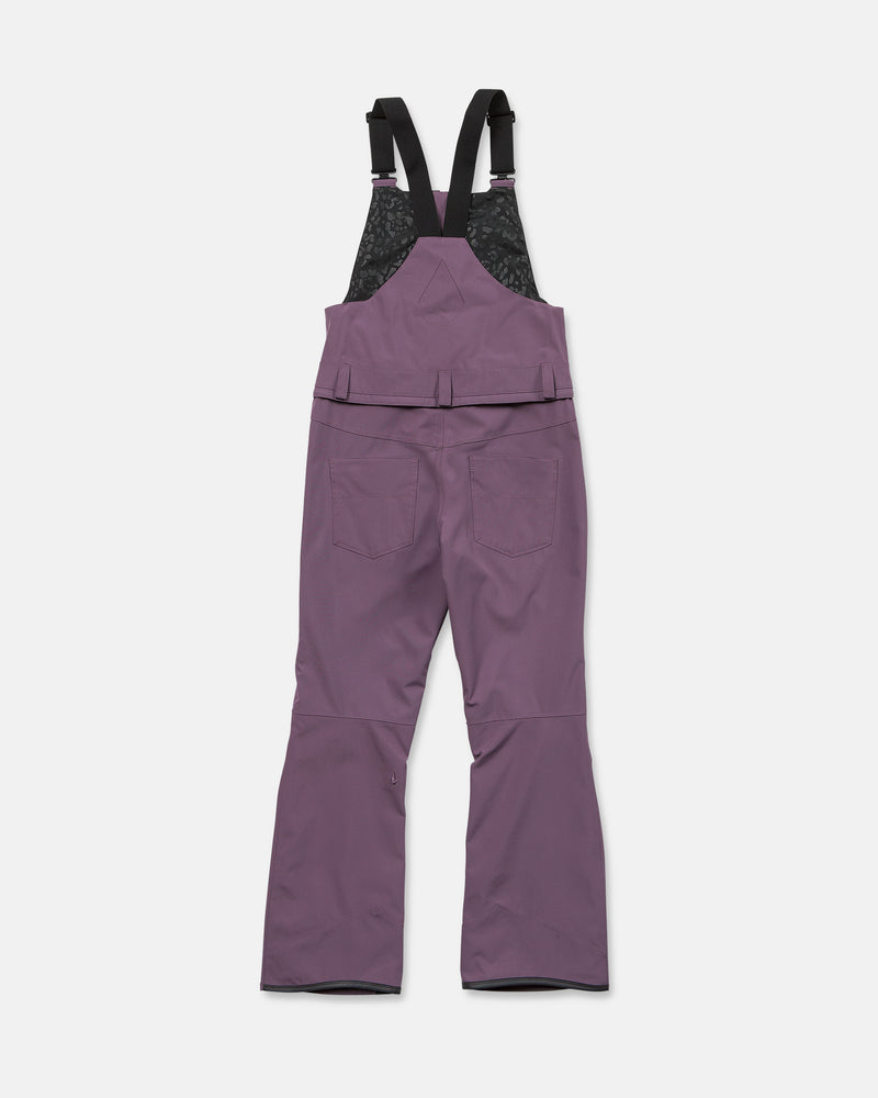 Volcom Women’s Swift Bib overall snow pants in purple, featuring black adjustable shoulder straps and two back pockets, are crafted from recycled fabric for a sustainable choice. Shown flat on a white background and viewed from the back, these waterproof pants offer both comfort and performance.
