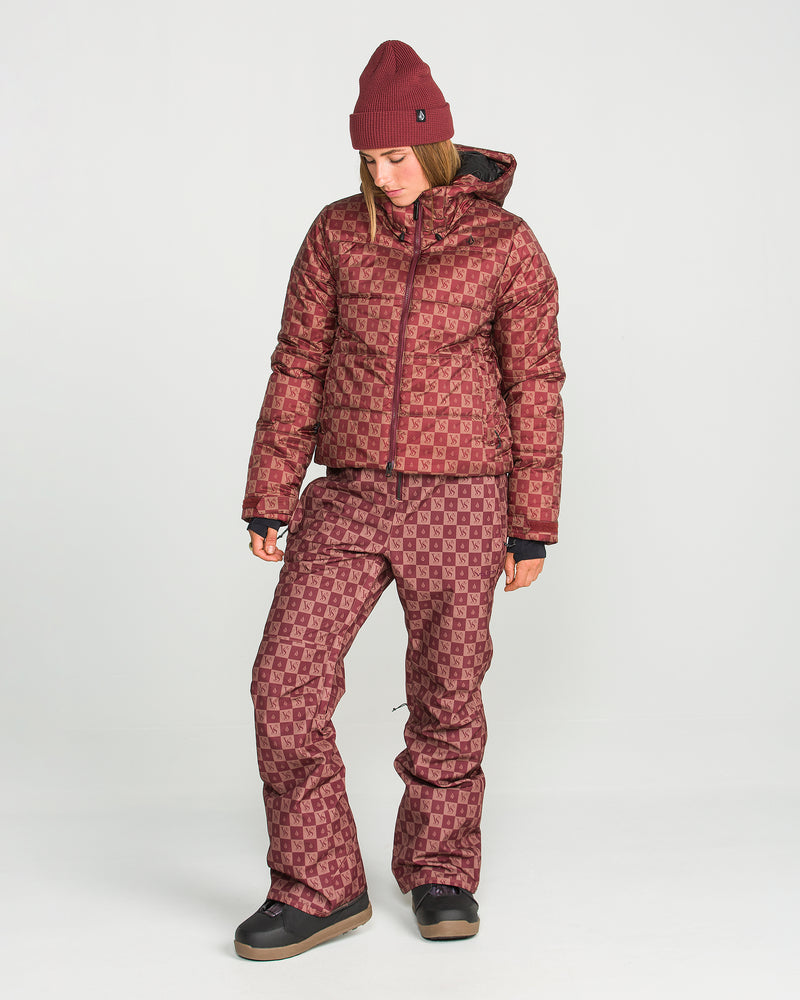 A person wearing the Volcom Women’s Swift Bib—a maroon beanie, a patterned maroon jacket, and matching pants crafted from recycled fabric—stands against a plain white background, looking down with their hands by their sides.