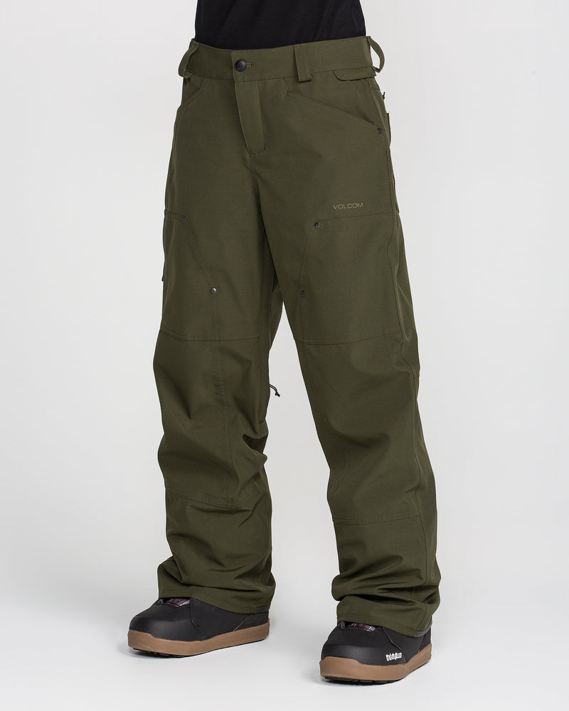 A person is shown from the waist down, standing against a plain white background, wearing Volcom Women’s Pollock Baggy Pants in olive green paired with black snow boots.