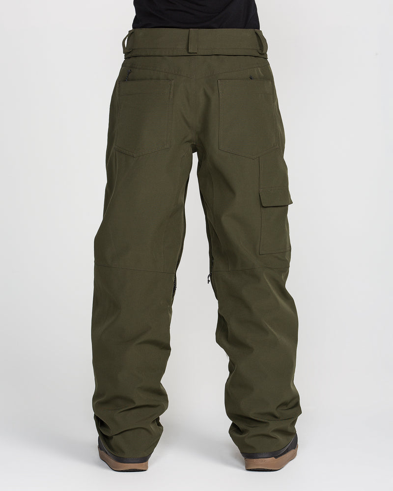 A person is photographed from behind against a plain white background, wearing Volcom Women’s Pollock Baggy Pants in olive green and black shoes. The pants feature large back and side pockets.