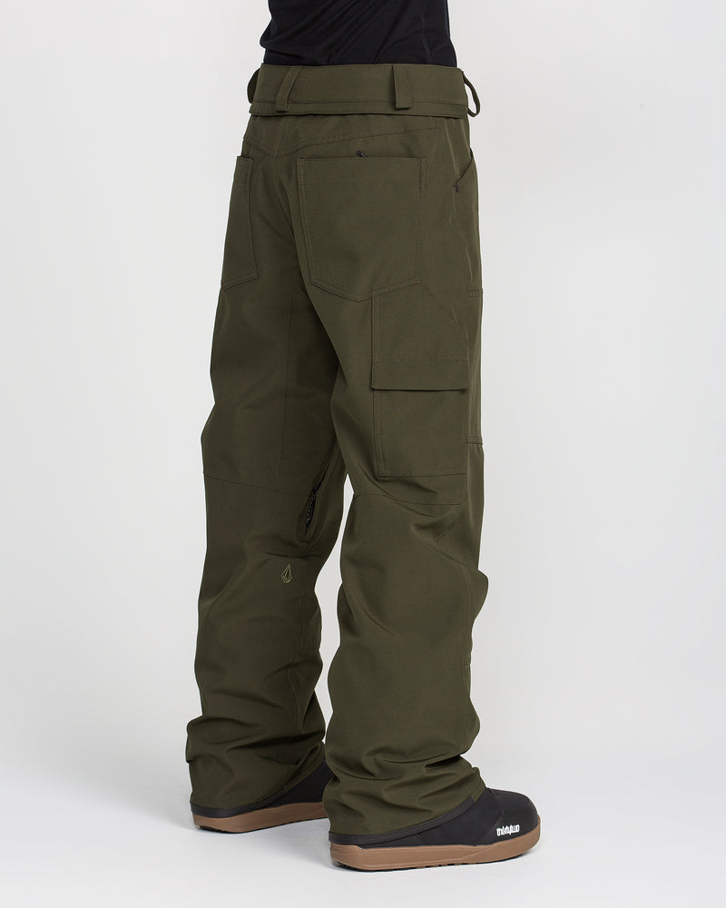 A person is wearing Volcom Women’s Pollock Baggy Pants in olive green along with black snowboard boots, standing against a white background. The waterproof pants feature multiple pockets and a loose, relaxed fit, making them ideal for outdoor or winter sports activities.