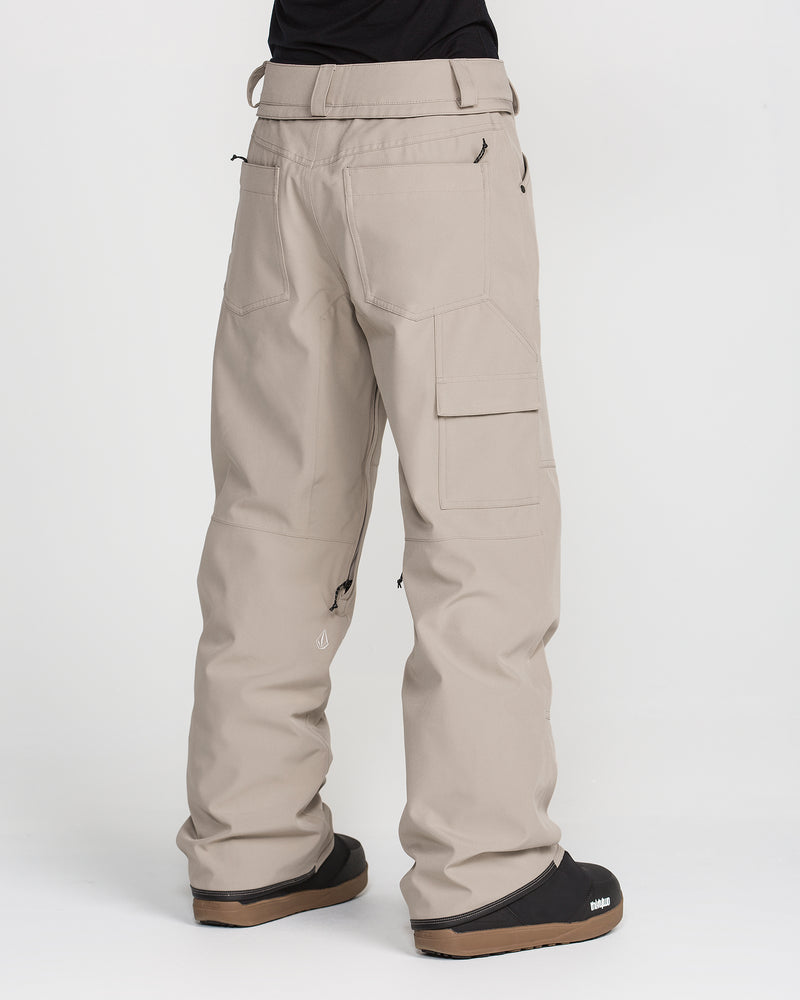 A person is shown from the back against a plain white background, wearing Volcom Women’s Pollock Baggy Pants in light beige—with multiple cargo pockets—and black shoes.