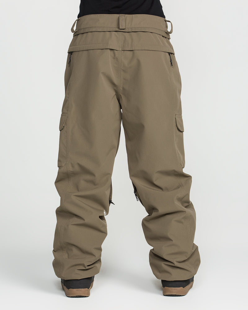 A person is wearing Volcom’s Unisex Liftline 20K Pants in brown—crafted from recycled fabric—paired with brown shoes, standing against a plain white background; the upper body is not visible.