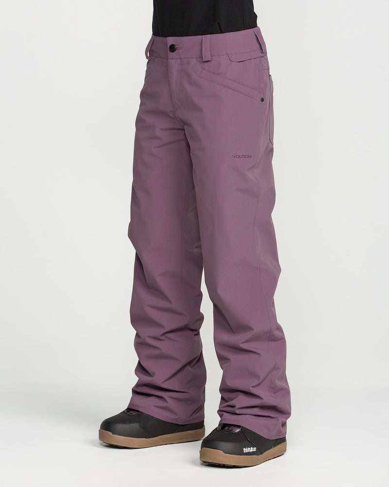 A person is wearing Volcom Women’s Stoned Pants in a slim mid-rise fit, paired with black snow boots, standing against a plain white background. Only the lower half of the body is visible.