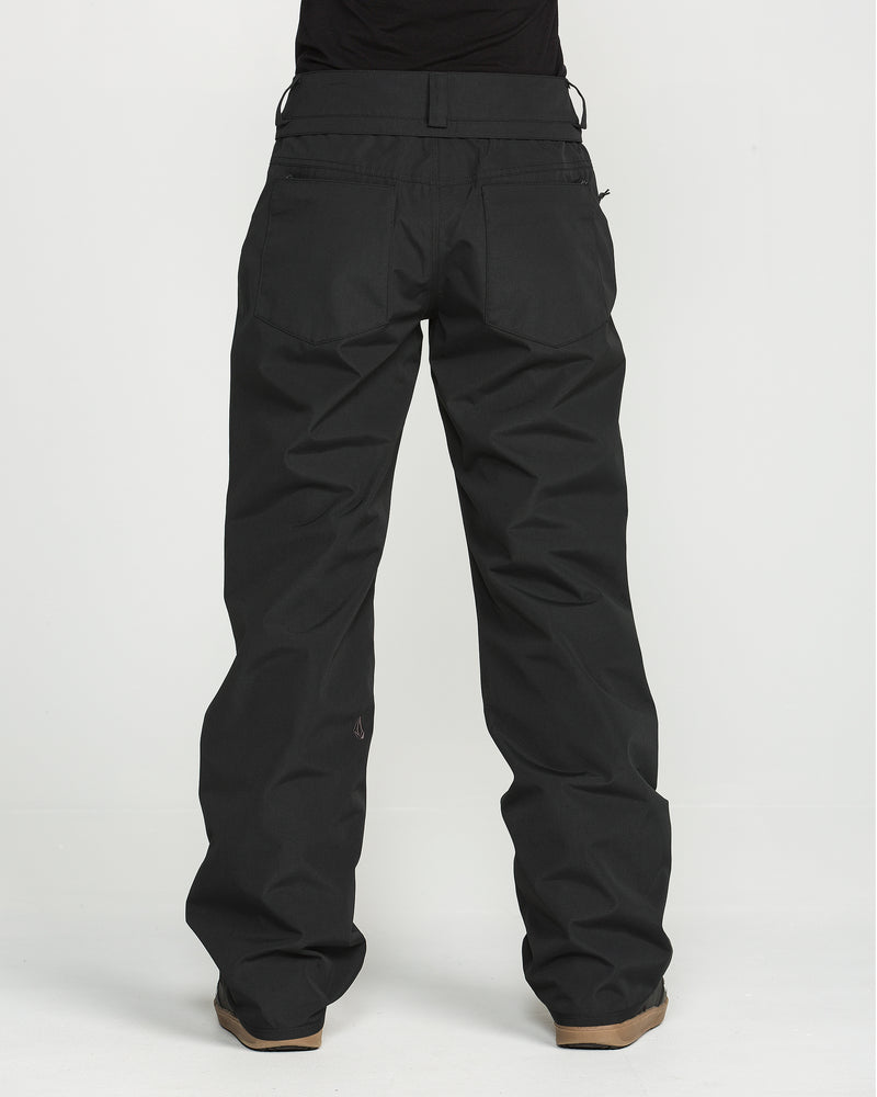 A person wearing Volcom Women’s Stoned Pants—loose-fitting black pants with a V-Science 2-Layer construction for waterproof performance—paired with brown shoes, stands against a plain white background. Only the person’s lower back and legs are visible; the upper body is not shown. These stylish yet practical women’s pants are designed for comfort and protection.