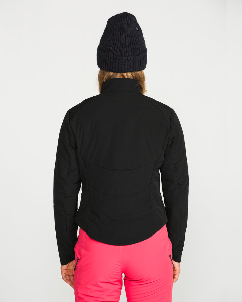 A person is seen from behind against a plain white background, wearing a black beanie, bright pink pants, and the Volcom Women’s Evergreen Full Zip Jacket in black.