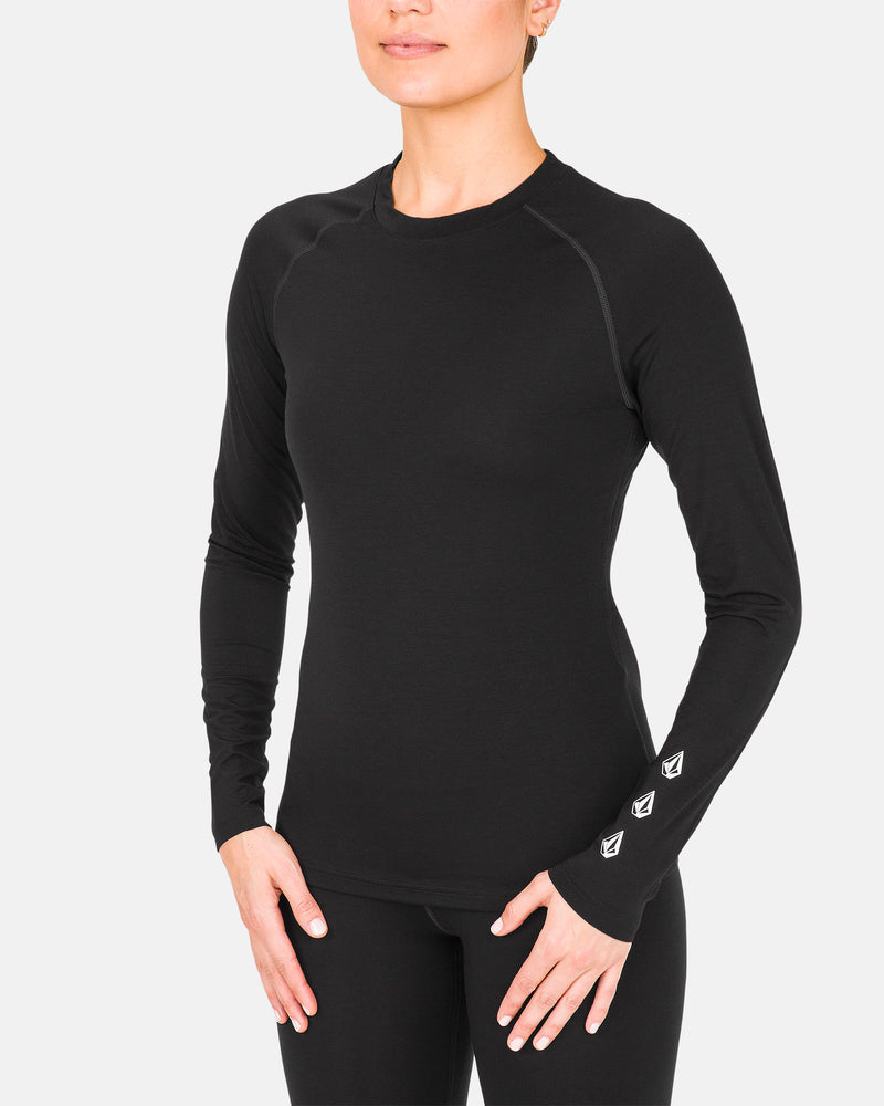 A person is wearing the Volcom Women’s W Merino Blend Crew— a fitted black long-sleeve athletic shirt— paired with black leggings, standing against a plain white background with their hands resting at their sides.