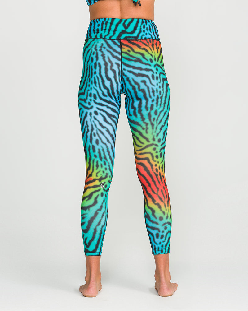 A person is shown barefoot from the back, wearing Volcom Women’s W V-Science Pants—high-waisted, ankle-length pants featuring a vibrant zebra stripe pattern in blue, green, red, and yellow. Crafted from quick-dry knit for Thermal Defense Layering, the pants are displayed against a white background.