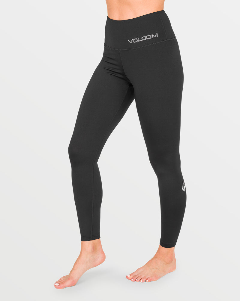 A person is shown from the waist down, barefoot, standing on a white background and wearing high-waisted black Volcom Women’s W V-Science Pants. The Volcom logo appears on both the waistband and the lower left leg.