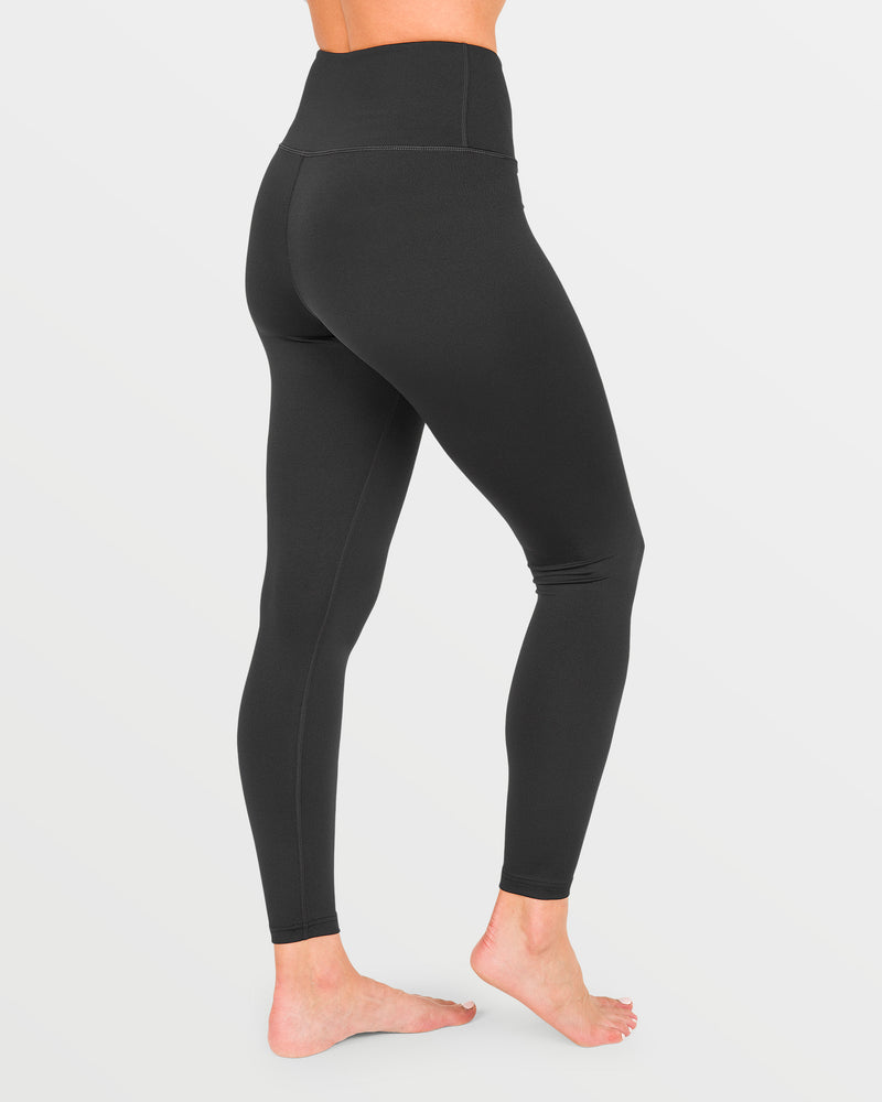 A person stands barefoot on a white background, modeling the Volcom Women’s W V-Science Pants in black with a high-waisted, quick-dry design, displaying side and back views from the waist down.