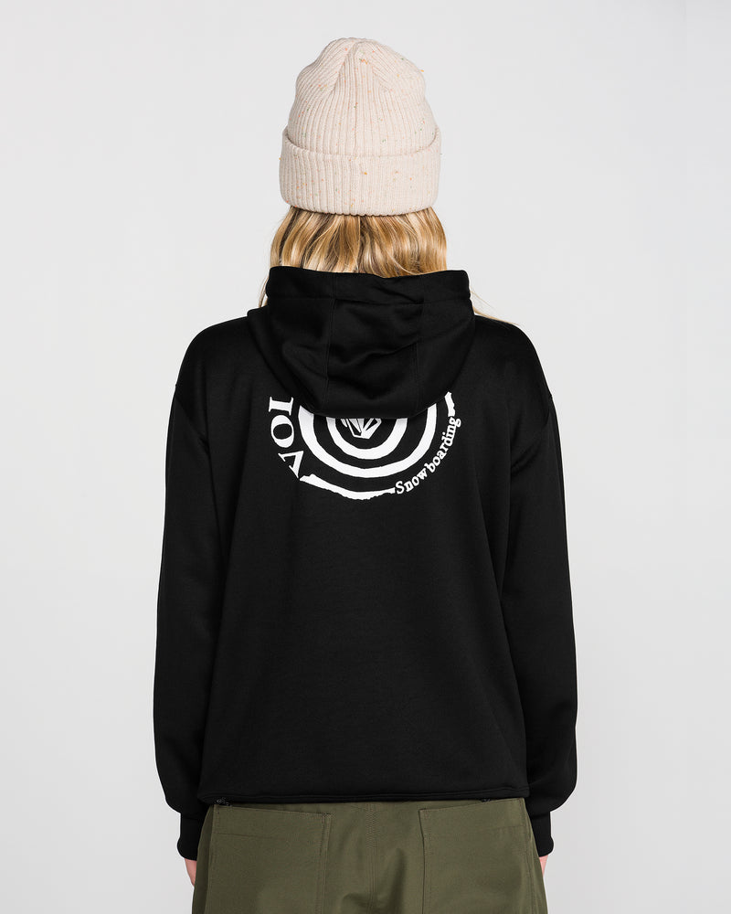 A person is seen from behind wearing a beige beanie, olive-green pants, and the Volcom Women’s Riding Hydro Pullover Hoodie in black, featuring a white circular graphic on the back, standing against a plain background.
