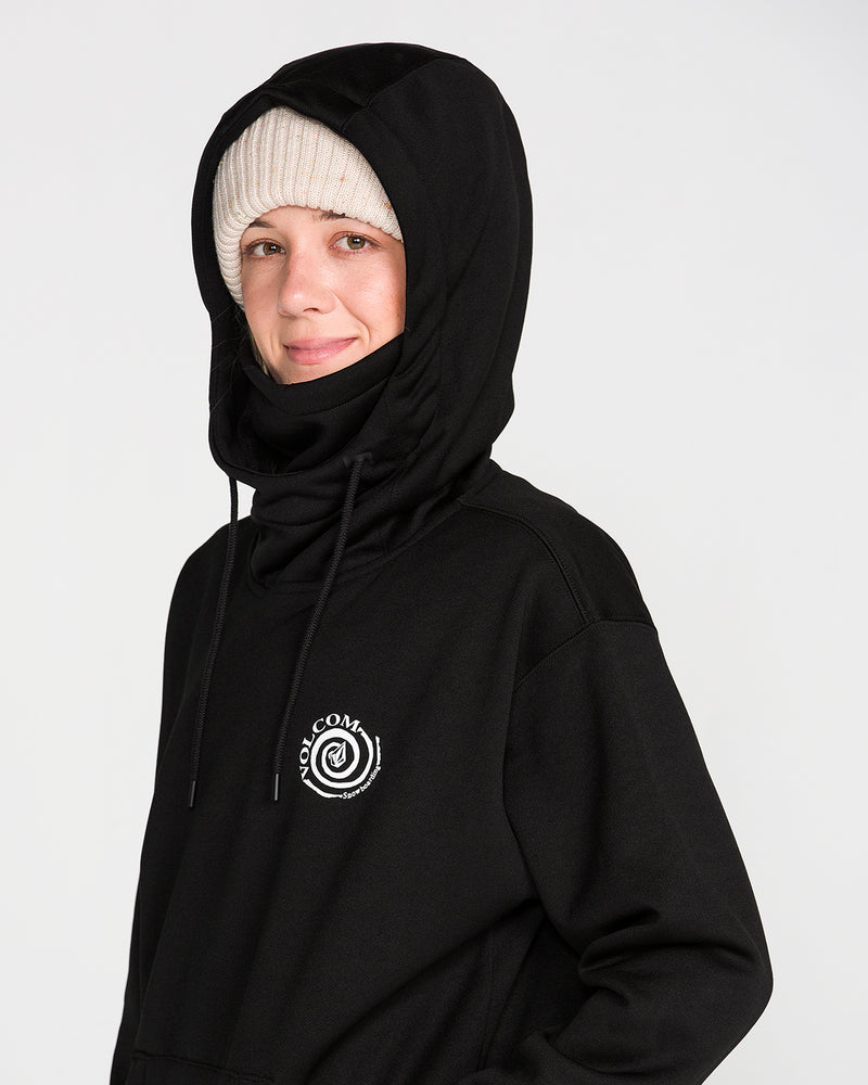 A woman wears the Volcom Women’s Riding Hydro Pullover Hoodie in black, featuring a white logo, along with a beige knit beanie. She smiles slightly while facing the camera against a plain white background.