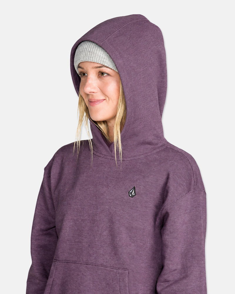 A person wearing the Volcom Women’s Alpine All Day Pullover—a purple hoodie with a subtle logo and a cozy handwarmer pocket—paired with a gray knit beanie, smiles and looks to the side against a plain background.