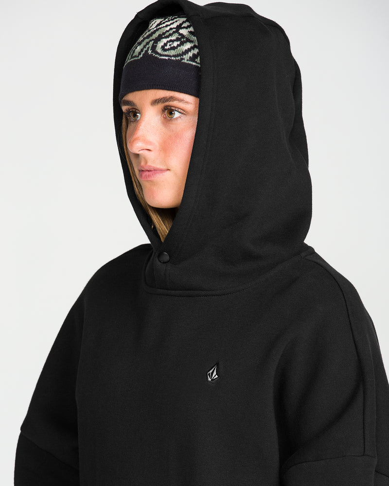 A person wearing the Volcom Women’s Yourfav Baggy Pullover in black and a patterned beanie, looking to the side with a neutral expression against a light background.