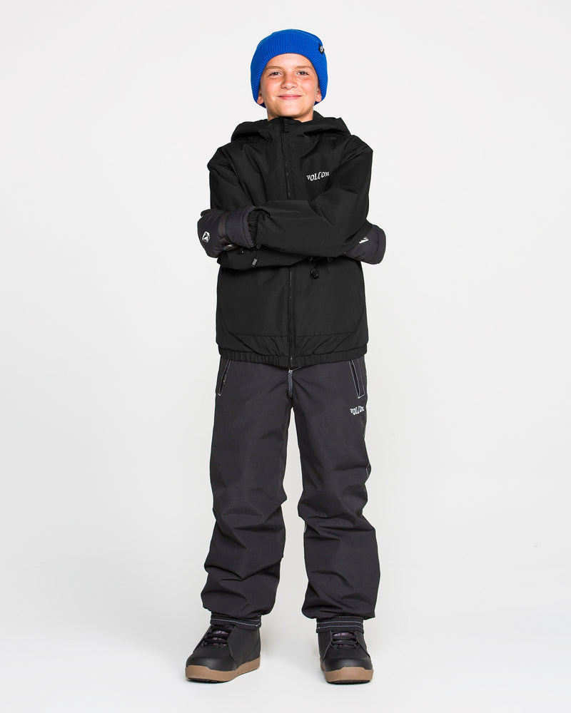 A smiling child wearing a blue beanie, dark pants, and the Volcom Kids’ Youth Chaos Insulated Jacket in black—featuring weather defense and recycled insulation—stands with arms crossed against a plain white background.