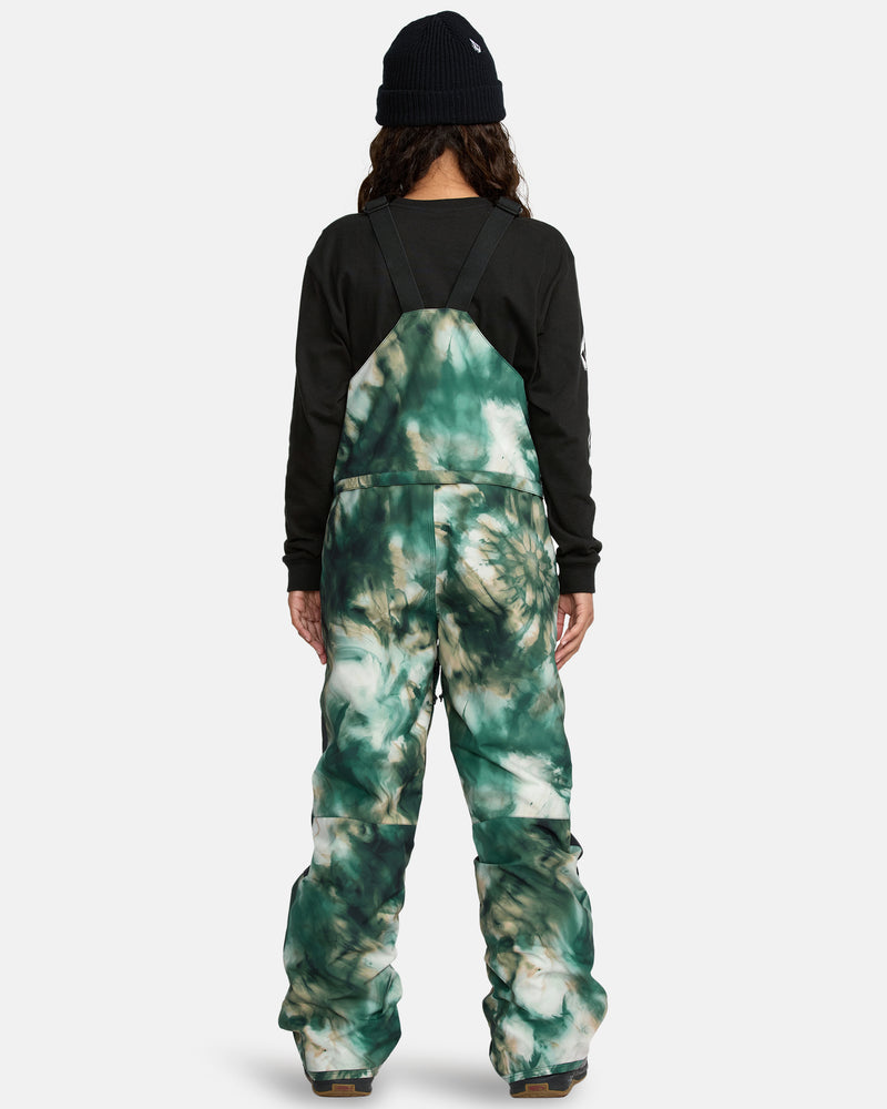 A person faces away, wearing a black beanie, black sweatshirt, and green and white tie-dye Kids' Barkley Insulated Bib Overall. The background is plain and light-colored.