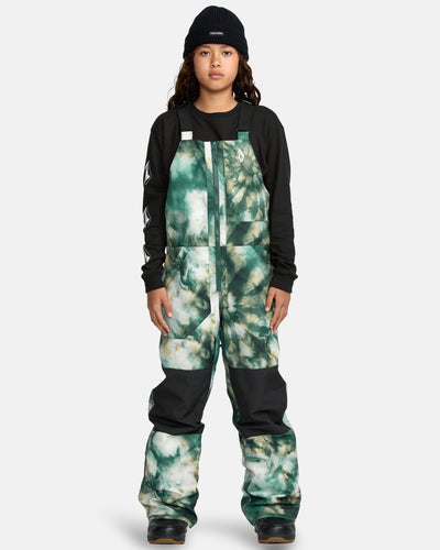 A child models the Kids' Barkley Insulated Bib Overall in green-and-white tie-dye, paired with a black beanie and black long-sleeve shirt, standing against a plain light gray background.