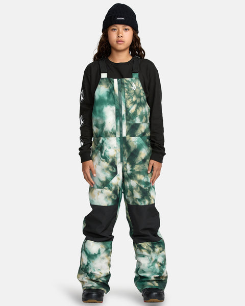 A child models the Kids' Barkley Insulated Bib Overall in green-and-white tie-dye, paired with a black beanie and black long-sleeve shirt, standing against a plain light gray background.