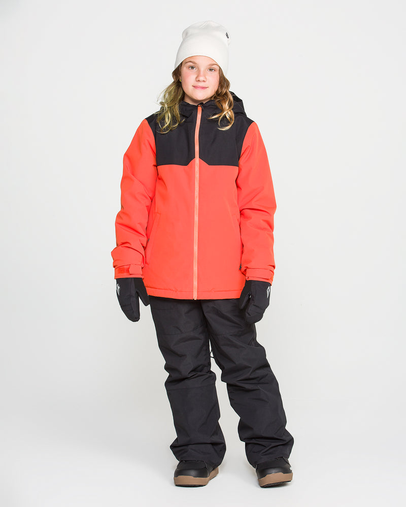 A child in a red and black winter jacket, Volcom Kids’ Youth Barkley Insulated Bib snow pants, black gloves, brown boots, and a white beanie stands facing forward against a plain white background.