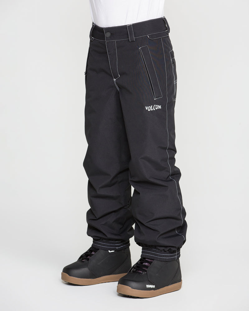 A child is shown wearing black Volcom Kids’ Youth Chaos Insulated Pants and black snow boots, standing against a plain white background. The pants are detailed with visible white stitching and display the Volcom logo on the left thigh. Featuring 10K/10K weather protection and recycled insulation for warmth and durability. Upper body is not visible.