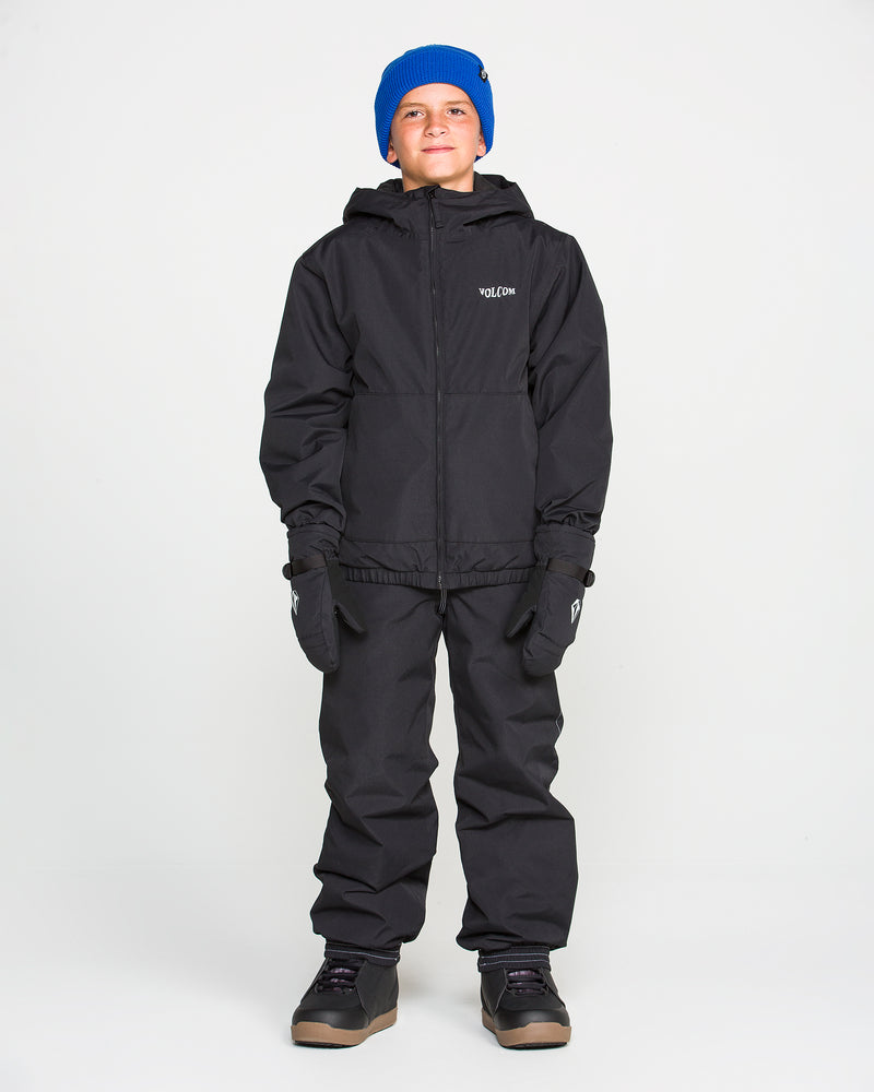 A person wearing a black hooded jacket, Volcom Kids’ Youth Chaos Insulated Pants with 10K/10K protection, black gloves, and a blue beanie stands and smiles in front of a plain white background.