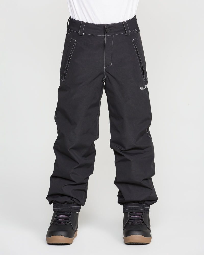 A person stands against a plain white background wearing Volcom Kids’ Youth Chaos Insulated Pants in black with recycled insulation, black winter boots, and a white shirt.