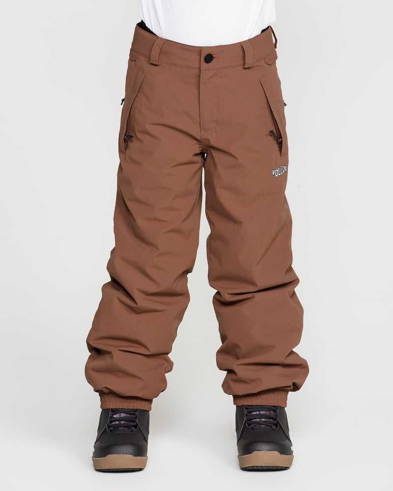 A person wearing Volcom Kids’ Youth Chaos Insulated Pants in brown, featuring recycled insulation and side pockets, along with black snow boots, stands against a plain white background.