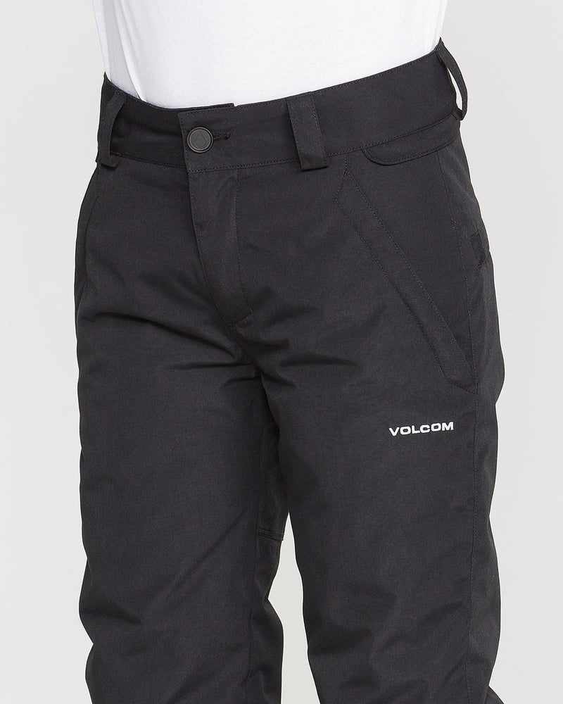 A person is shown from the waist to mid-thigh wearing a white shirt and black Volcom Kids’ Youth Freakin Chino Insulated Pants. The pants feature an adjustable waist for a customizable fit, button closure, belt loops, a side pocket, and display the Volcom logo on the upper left thigh.