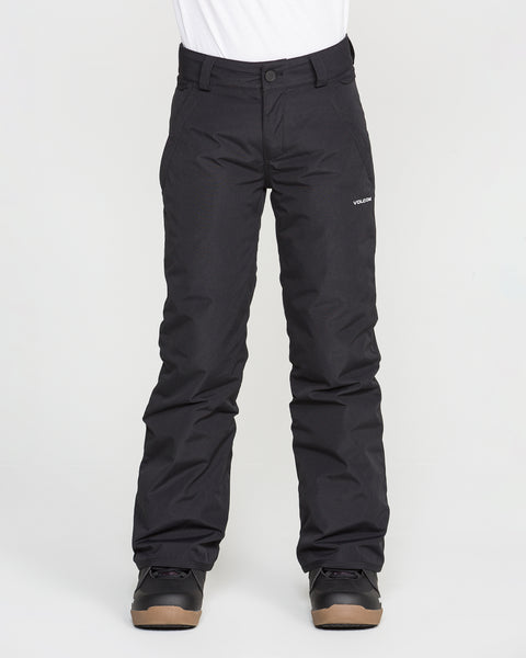 A person wearing black Volcom Kids’ Youth Freakin Chino Insulated Pants with an adjustable waist and black boots stands against a plain white background. The waterproof, breathable snow pants feature a small white Volcom logo on the left thigh. The person’s upper body is not visible.
