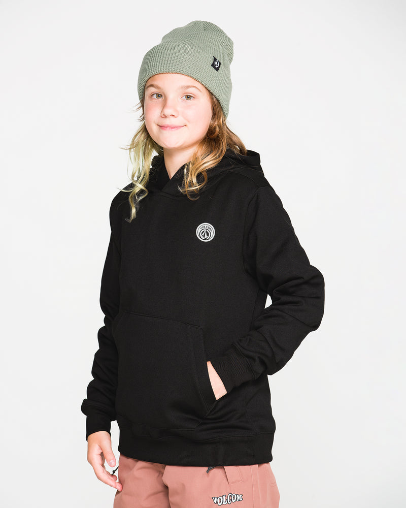 A young person wearing a gray beanie, pink pants, and the Volcom Kids’ Youth Hydro Fleece Hoodie—featuring a small circular logo and made from hydrophobic fleece—stands with one hand in their pocket, smiling in front of a plain white background.