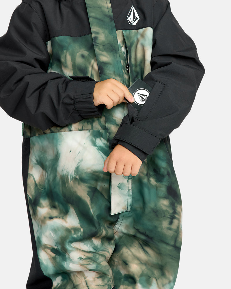 A child wearing the Kids' Little Flurry One Piece in black and green tie-dye adjusts a Velcro strap on the sleeve. The Volcom logo appears on the chest and sleeve, with the child's face out of view.