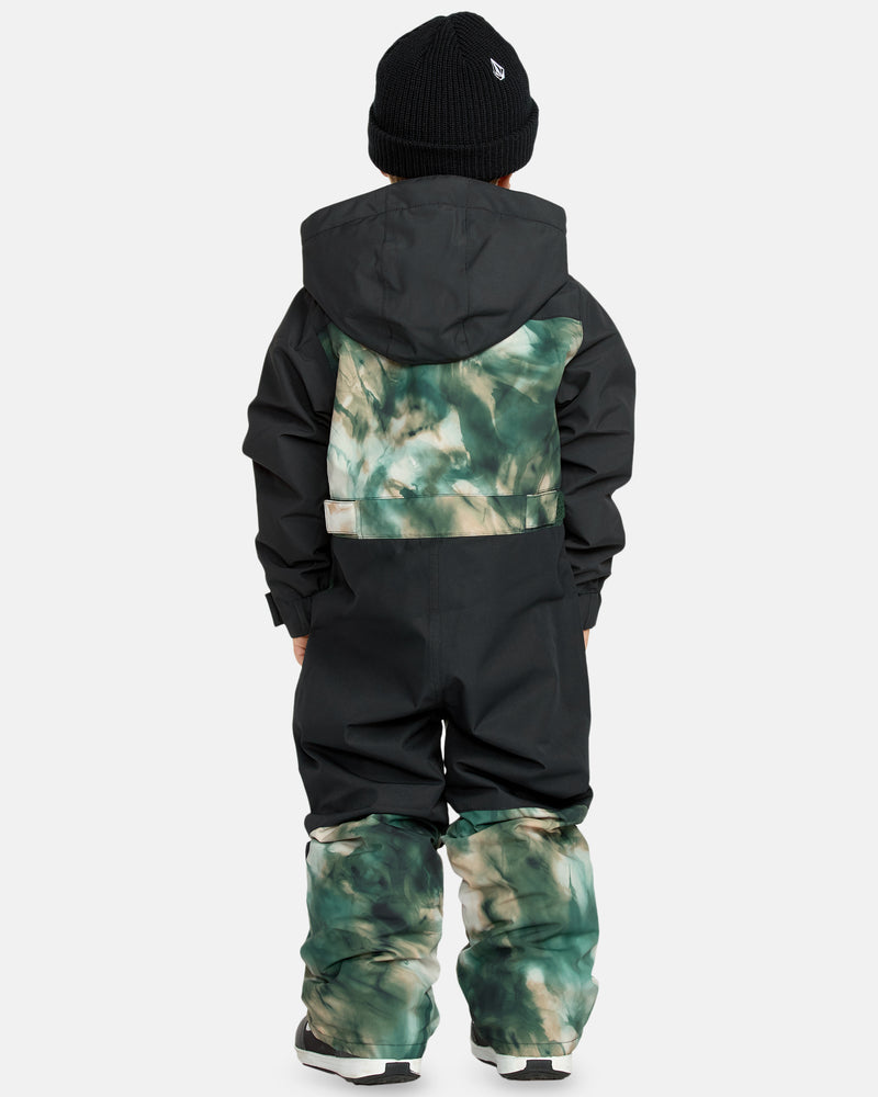 A child stands facing away, wearing the Kids' Little Flurry One Piece—a hooded snowsuit with black sleeves and green tie-dye sections—and a black beanie. Their hands rest by their sides.