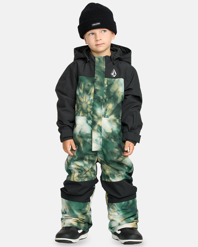 A young child stands against a plain light background, wearing the Kids' Little Flurry One Piece in black and green tie-dye with a hood, paired with a black beanie and black snow boots, looking slightly to the side.