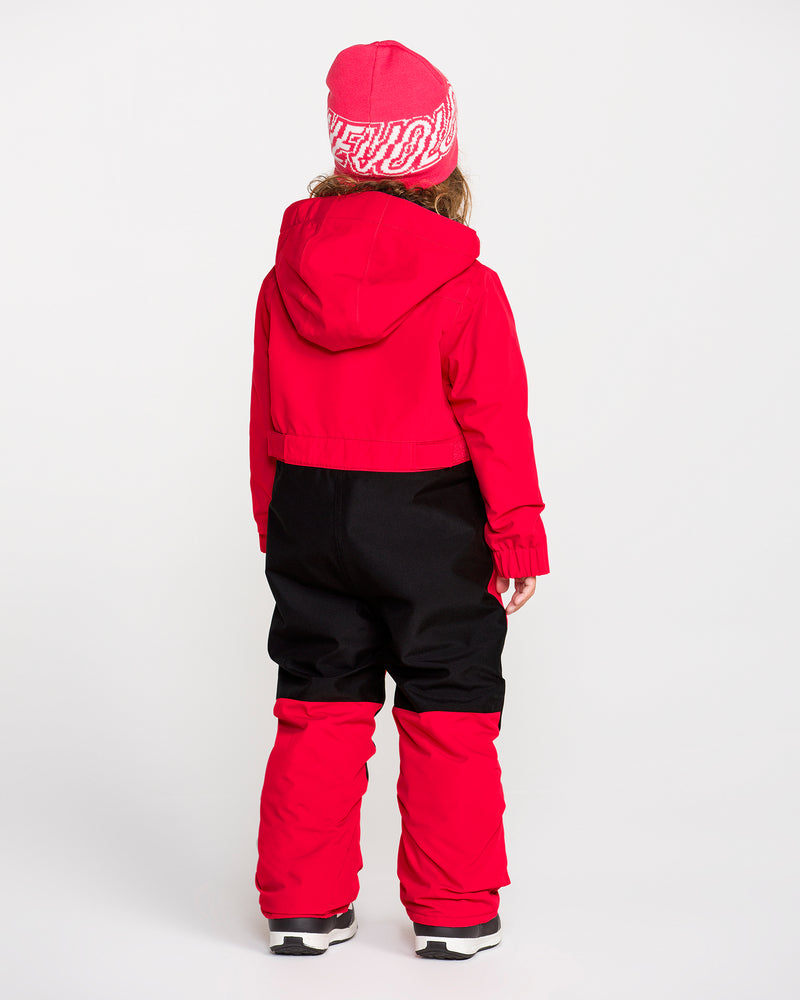 A child in a red hooded jacket, red and black snow pants, and a red beanie stands facing away against a plain white background, showcasing the Volcom Kids’ Little Flurry One Piece—insulated and crafted from recycled V-Science fabric with reliable 10K/10K protection.