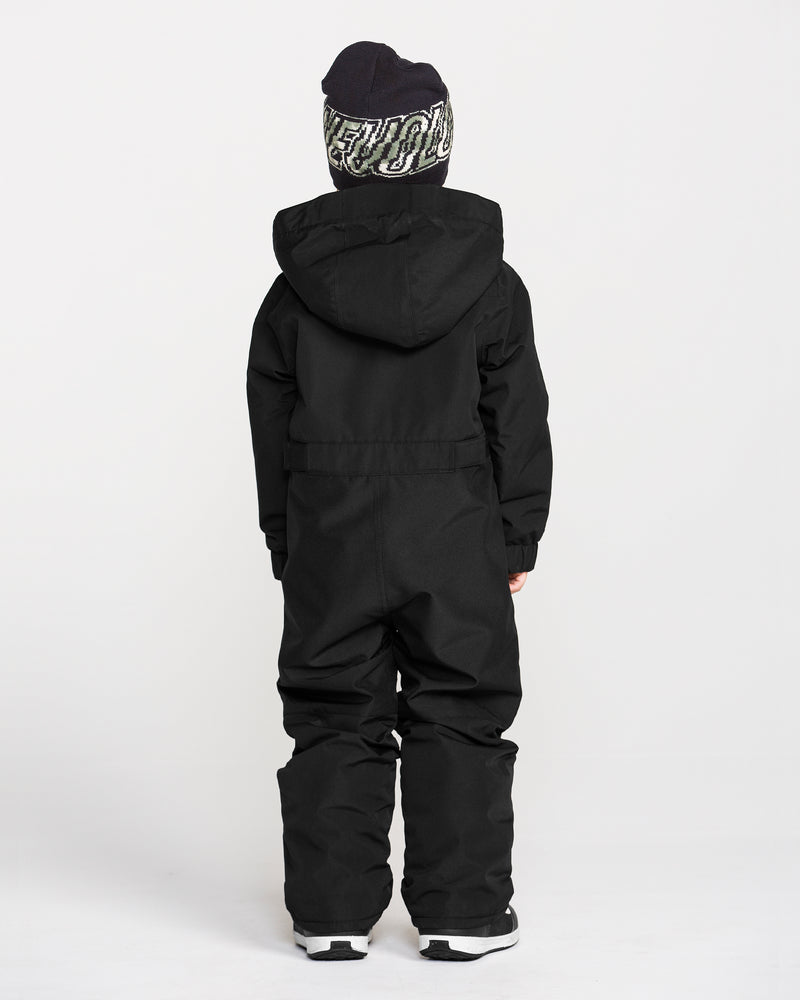 A child wearing the Volcom Kids’ Little Little Flurry One Piece Snow Suit and a black and white beanie stands with their back to the camera against a plain white background.