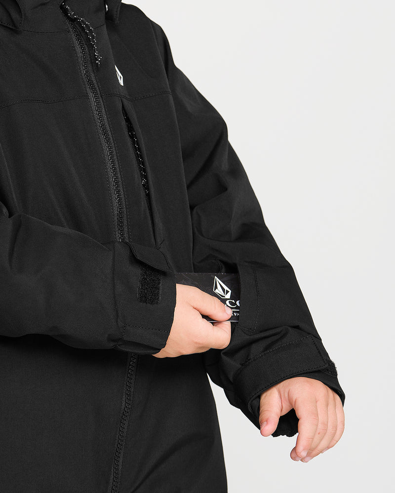 A person adjusts the Velcro cuff of a Volcom Kids’ Little Flurry One Piece Snow Suit sleeve, with only their hands and part of the suit visible against a light background.