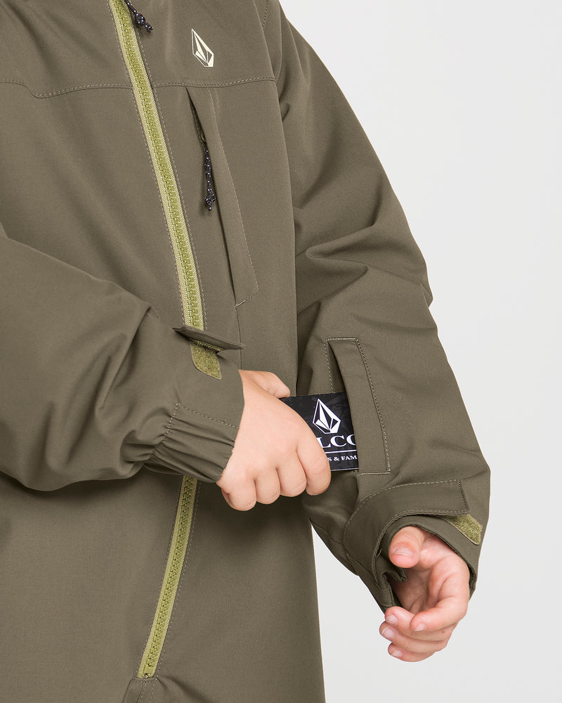 A child wearing the Volcom Kids’ Little Flurry One Piece in olive green places a black Volcom tag into a sleeve pocket. The one piece showcases zippered details and a small Volcom logo on the chest, crafted from recycled V-Science fabric for sustainable style.