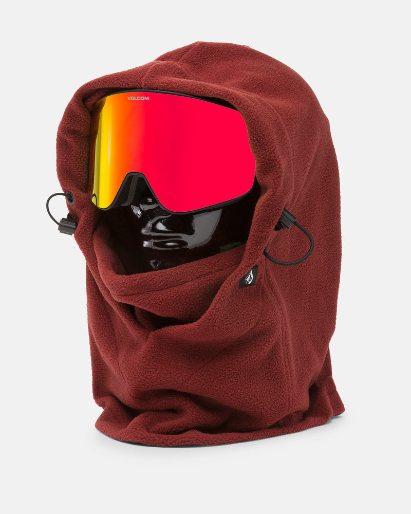 A black mannequin head displays the Volcom Women’s V.Scout Hood in red, featuring an adjustable toggle, fleece neck warmer, and side drawstrings, paired with reflective red ski goggles, all set against a plain white background.