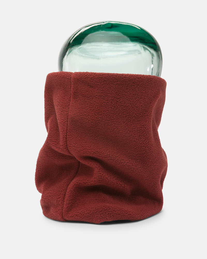 A green glass jar is wrapped in a red Volcom Women’s V.Scout Neckband, covering most of its surface except the top. The soft neckband-like wrap adds a sense of warmth to the plain white background.